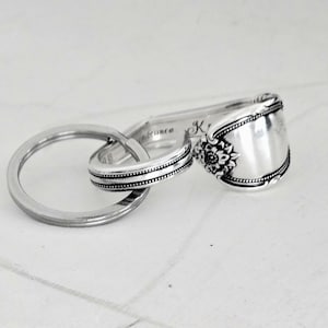 May include: A set of three silver rings, one a large circle, the other two crafted from silverware. One ring features a spoon bowl with floral detailing. The word "embrace" is engraved on the silverware.