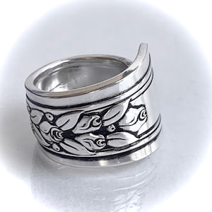 May include: A silver ring with a floral design. The ring is wide and has a curved band.