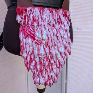 May include: A pink and white faux leather dragon scale belt piece. The scales are raised and have a textured finish.