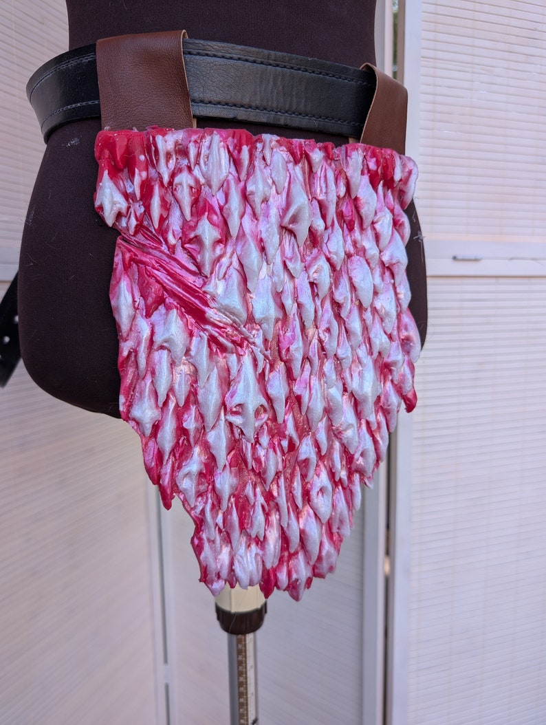 May include: A pink and white faux leather dragon scale belt piece. The scales are raised and have a textured finish.