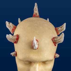 Könnte beinhalten: Ein weißer Mannequin-Kopf mit sieben weißen und roten Hörnern, die oben angebracht sind. Die Hörner sind spitz und haben eine raue Textur.