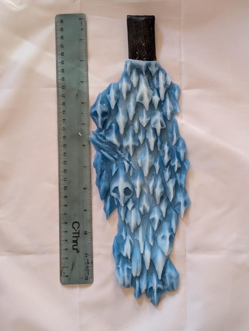 May include: A blue and white ice sculpture with a brown leather handle. The sculpture is shaped like a jagged, pointed rock formation.