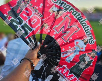 May include: A red and black graduation fan with the text "Class of 2023" and "Congratulations Amanti". The fan features images of a graduate in a cap and gown and other images of the graduate. The fan is held open.