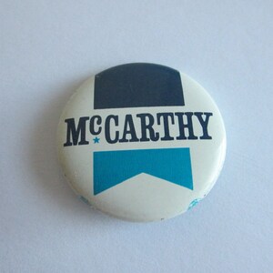 May include: White button with a blue and black design. The button says "McCarthy" with a star.