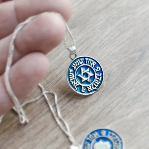 May include: A silver chain necklace with a blue and silver pendant featuring a Star of David and Hebrew text.