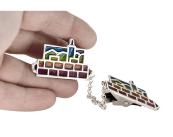 May include: A silver-toned talit clip with a colorful enamel design depicting a cityscape. The clip has a chain connecting the two pieces.
