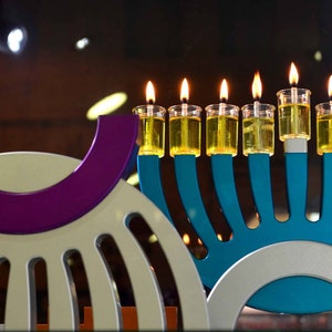 May include: A blue menorah with nine lit candles, each with a clear glass holder. The menorah is on a white and blue base. The menorah is in front of a white and purple object.