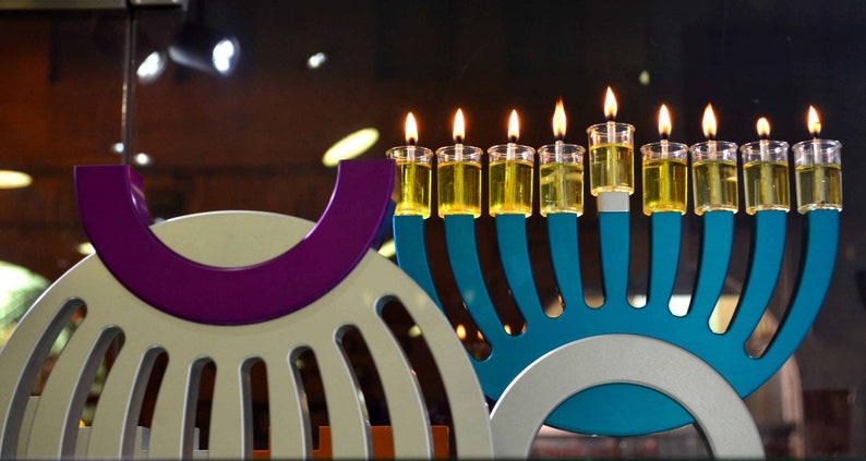 May include: A blue menorah with nine lit candles, each with a clear glass holder. The menorah is on a white and blue base. The menorah is in front of a white and purple object.