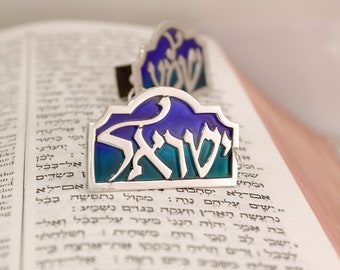 May include: Two silver mezuzah cases with blue and green enamel. The Hebrew word "Shabbat" is written on the cases.