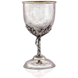 May include: A silver Kiddush cup with a hammered finish and a tree-like stem with leaves. The cup has a gold rim.