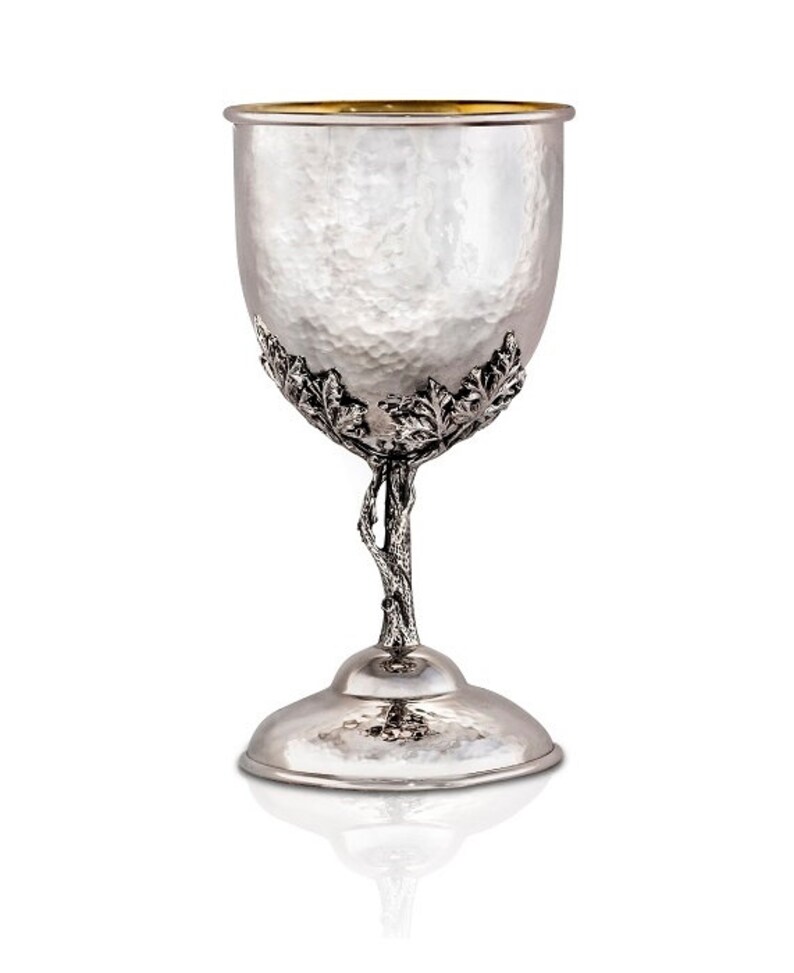 May include: A silver Kiddush cup with a hammered finish and a tree-like stem with leaves. The cup has a gold rim.