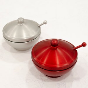 May include: Two small, round, lidded bowls with matching spoons. One bowl is silver and the other is red.