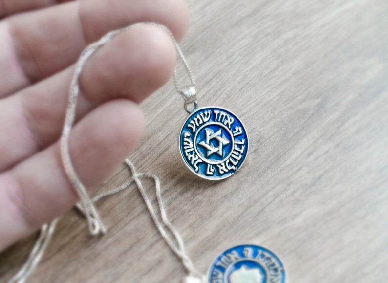 May include: A silver chain necklace with a blue and silver pendant featuring a Star of David and Hebrew text.