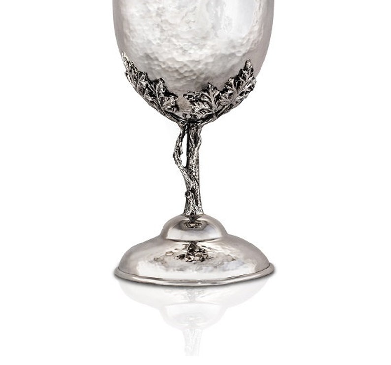 May include: A silver goblet with a hammered finish and a tree-like stem with leaves. The goblet has a wide base and a rounded bowl.