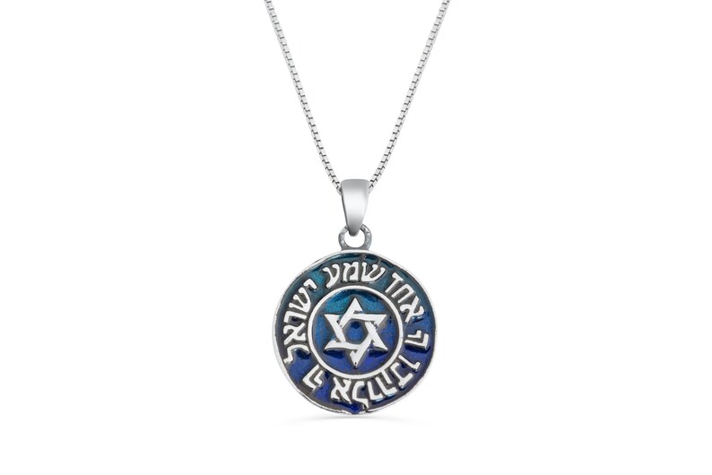 May include: A silver necklace with a blue enamel pendant featuring a Star of David and Hebrew text. The pendant is round and has a blue and white gradient.