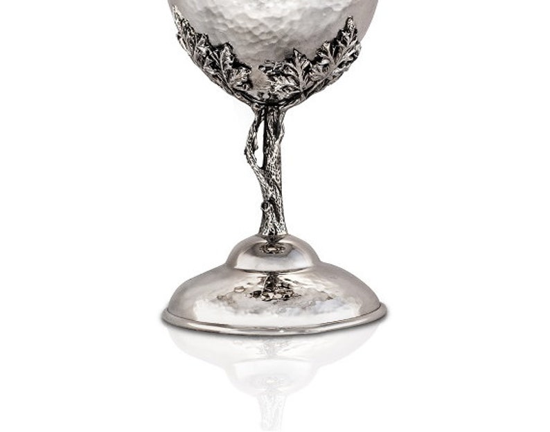 May include: Silver goblet with a hammered finish and a tree branch design. The goblet has a wide base and a round bowl.