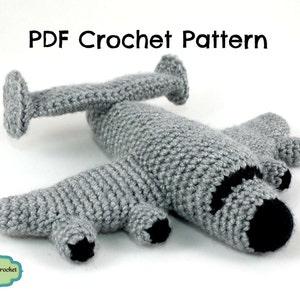 May include: A gray crocheted airplane toy with black details. The toy is lying on a white surface. PDF Crochet Pattern.