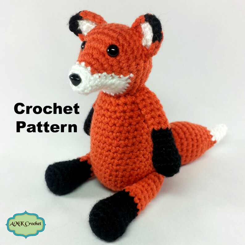 May include: Crochet pattern for a sitting fox amigurumi. The fox is orange with black ears, paws, and tail accents. The fox has white on its muzzle and the tip of its tail.