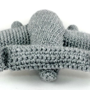 May include: A grey crocheted airplane toy with a long wingspan and a rounded body. The airplane is made with a single crochet stitch and has a textured surface.