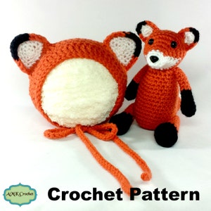 May include: A crochet pattern for a fox hat and a small fox plushie. The hat is orange with white ears and a white lining. The plushie is orange with black ears, a black nose, and black feet.