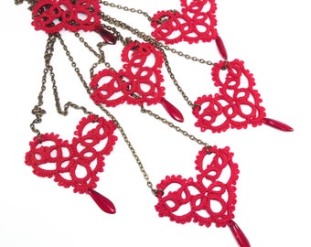 May include: A necklace with six red crocheted hearts hanging from a chain. Each heart has a red bead at the bottom.