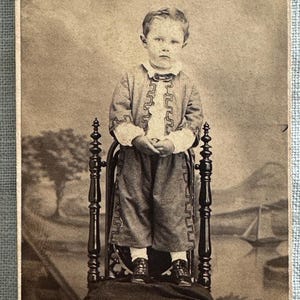CDV / Carte de visite of a boy standing on a chair. Painted studio backdrop