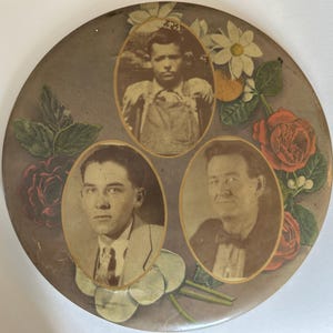May include: A vintage, round decorative piece featuring three sepia-toned portraits in oval frames. The background is a muted gray with painted floral accents, including red roses, white daisies, and green leaves. The portraits appear to be of men.