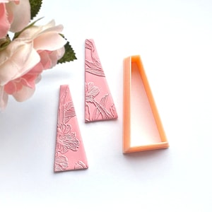 May include: Two pink triangle-shaped polymer clay earrings with a floral design and a matching orange plastic mould.