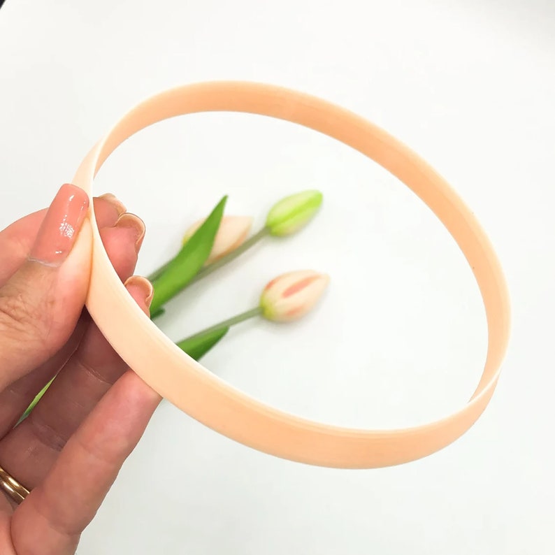 May include: A peach-colored headband made of a soft, flexible material. The headband is shown being held by a hand.