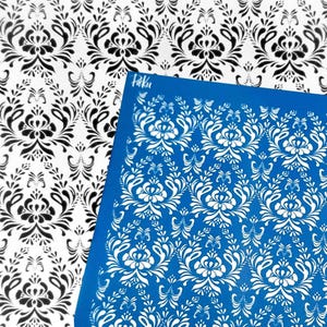 May include: A blue stencil featuring a white floral damask design is shown beside a white and black damask patterned paper. The stencil has the word "Paku" printed on it. The damask pattern is a classic design.