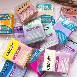May include: A selection of colourful polymer clay bars, each labelled 'Cernit Opaline' and featuring a product description in multiple languages. The clay bars are packaged in clear plastic wrappers.