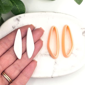 May include: Two pairs of earring moulds, one pair is white and the other pair is peach. The moulds are shaped like a teardrop.