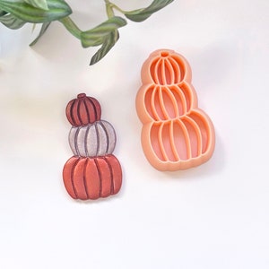 Può includere: Un set di tre tagliabiscotti a forma di zucca impilati. I tagliabiscotti sono in plastica arancione chiaro e sono progettati per creare una forma di zucca a strati.