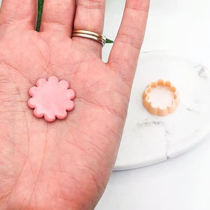 Puede incluir: Un cortador de galletas de color rosa en forma de flor y un cortador de galletas de color beige en forma de flor.