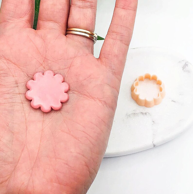 Puede incluir: Un cortador de galletas de color rosa en forma de flor y un cortador de galletas de color beige en forma de flor.