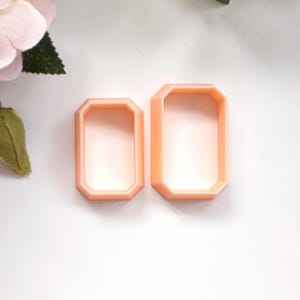 Pode incluir: Dois cortadores de biscoitos de plástico cor de pêssego em forma de octógono. O cortador maior está à direita e o menor à esquerda.