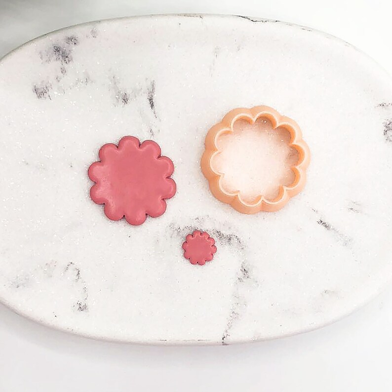 Puede incluir: Tres cortadores de galletas con forma de flor sobre una superficie de m&aacute;rmol blanco. El cortador m&aacute;s grande es de color marr&oacute;n claro, el mediano es de color rosa y el m&aacute;s peque&ntilde;o es de color rosa oscuro.