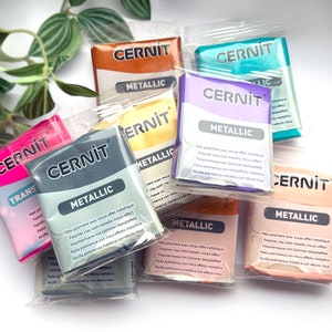 May include: A close-up of eight packages of metallic polymer clay. The packages are arranged in a pile, with the brand name "CERNIT" visible on each package. The clay is available in a variety of colours, including gold, silver, pink, purple, teal, and peach.