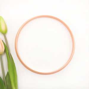 May include: A peach-colored embroidery hoop with a white background.