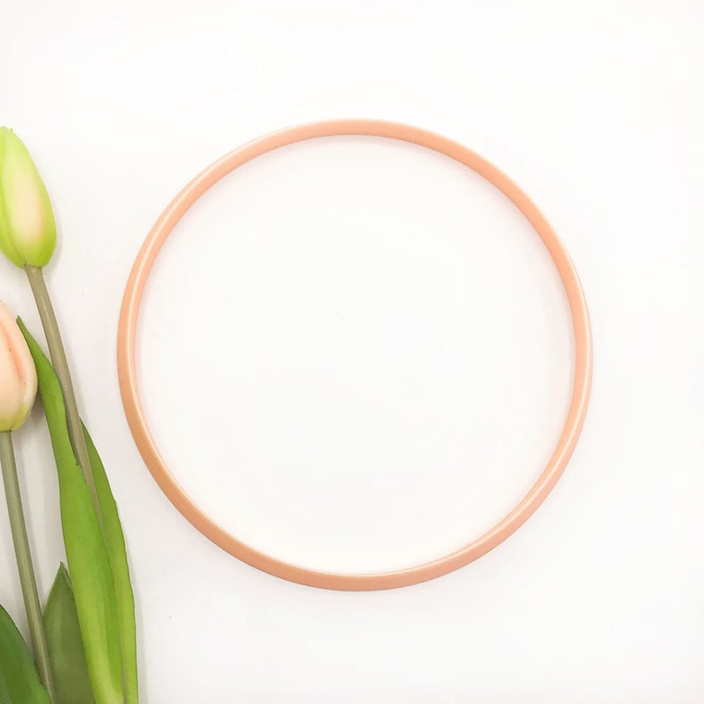 May include: A peach-colored embroidery hoop with a white background.