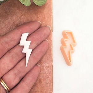 Può includere: Un tagliapasta a forma di fulmine in plastica bianca con un tagliapasta a forma di fulmine in plastica pesca accanto.