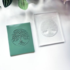 Op de afbeelding: Een transparante acryl stempel met een gedetailleerd ontwerp van een levensboom. De stempel wordt getoond naast een groene afdruk van het ontwerp.