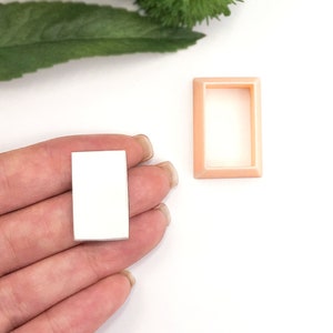 Puede incluir: Una bandeja rectangular blanca de resina en blanco con un marco de plástico melocotón. La bandeja está en la mano de una persona.