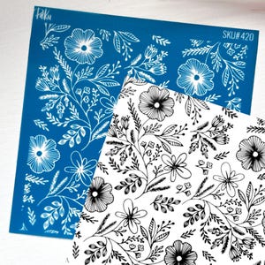 May include: A square blue stencil sheet with white floral line art and the text Paku and SKU# 420, layered over a white sheet with identical black floral line art. The design features various flowers, leaves, and stems in a repeating pattern.