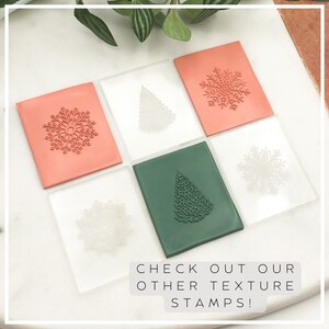 Op de afbeelding: Zes transparante acrylblokken met verschillende kerstthema-ontwerpen. De ontwerpen omvatten sneeuwvlokken en kerstboom. De blokken zijn gerangschikt in een rasterpatroon op een wit oppervlak. De tekst "CHECK OUT OUR OTHER TEXTURE STAMPS!" is onder de blokken afgedrukt.