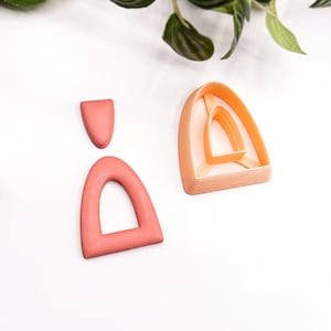 May include: A set of two pink polymer clay arch shapes. The larger arch has a smaller arch cut out inside of it. The smaller arch is a solid shape.