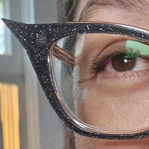 May include: A pair of black cat-eye glasses with glitter detailing on the frames. The glasses have clear lenses.