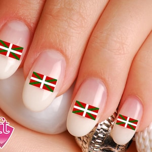 May include: Close-up of a hand with manicured nails. Each nail features a small sticker of the Basque flag, a red field with a white cross and green diagonal cross. The nails are oval-shaped and painted with a light, neutral color.