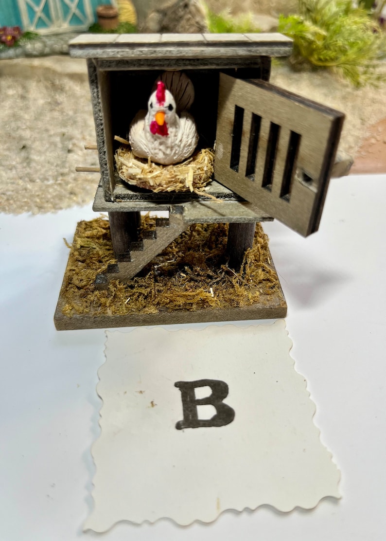 Puede incluir: Un gallinero de madera en miniatura con una gallina blanca en su interior. El gallinero tiene una peque&ntilde;a puerta que est&aacute; abierta y una escalera que lleva hasta el gallinero. El gallinero est&aacute; sentado sobre una cama de paja marr&oacute;n. La imagen tiene la letra "B" en una tarjeta blanca debajo del gallinero.