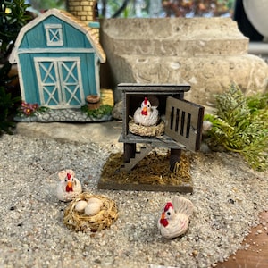 Puede incluir: Un gallinero de madera en miniatura con una gallina blanca dentro y dos gallinas blancas afuera. El gallinero tiene una peque&ntilde;a puerta de madera y una escalera. Hay tres huevos blancos en un nido fuera del gallinero.